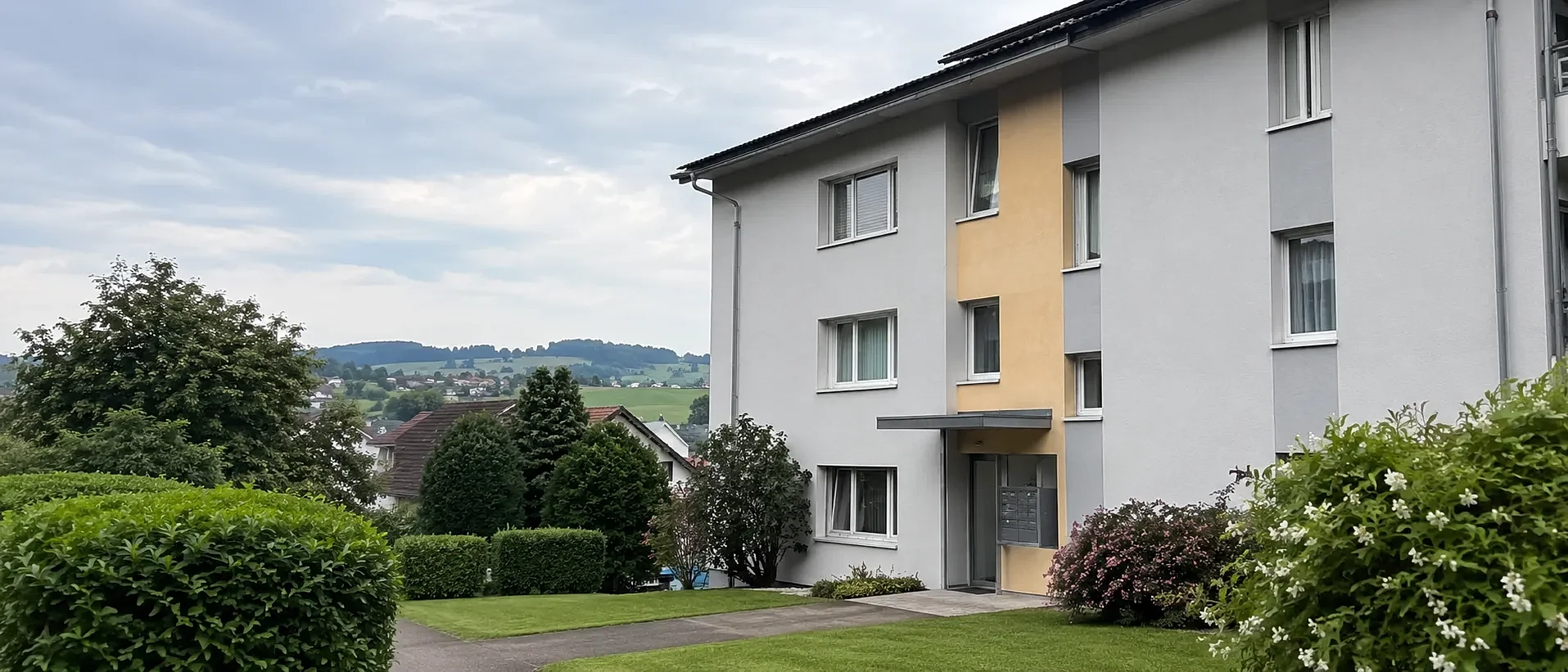 Gepflegte Wohnliegenschaft mit Garten und Hecke, im Hintergrund die Ostschweizer Hügellandschaft